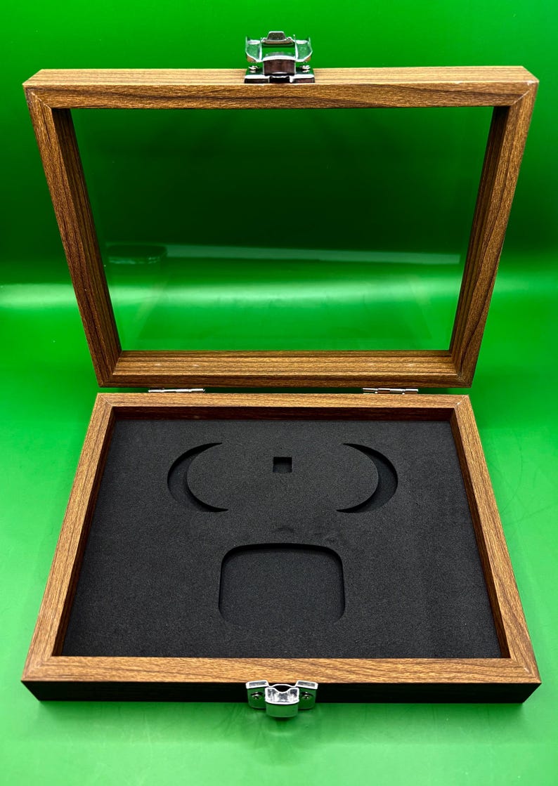 May include: Open wooden display case with a clear glass top and a black foam insert. The case has a hinged lid with a silver clasp. The interior foam has cutouts for displaying items. The wood has a natural grain.