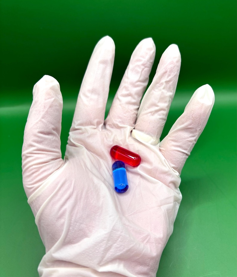 May include: Two capsules, one red and one blue, rest on a white gloved hand against a green background. The red capsule is oblong, while the blue one is cylindrical. The capsules are likely pharmaceutical products.