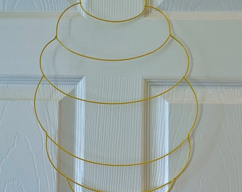 May include: A gold wire honeycomb wreath with six layers of wire circles. The wreath is hanging on a white door.