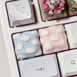 May include: A white keyboard with custom keycaps. The keycaps feature a cloud design in blue, pink, and white. The keyboard also has a keycap with the text "Love As" in pink and white.