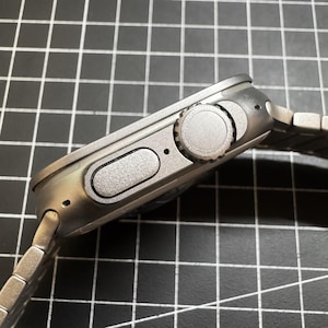 Peut inclure: Une montre-bracelet argentée avec un bouton rond texturé sur le côté. La montre a un bracelet en métal argenté.