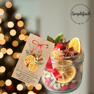Puede incluir: Un tarro de vidrio lleno de rodajas de naranja secas, palitos de canela, anís estrellado y otras especias. Una cinta roja y una etiqueta marrón con el texto "Christmas Simmering Potpourri" están atados al tarro.