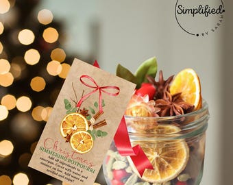 May include: A glass jar filled with dried orange slices, cinnamon sticks, star anise, and other spices. A red ribbon and a brown tag with the text "Christmas Simmering Potpourri" are attached to the jar.