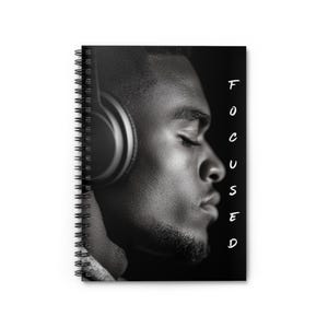 May include: Spiral-bound notebook with a black and white image of a person wearing headphones. The person has their eyes closed. The word "FOCUSED" is written vertically in white on the right side of the notebook.