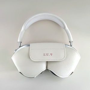 May include: White leather headphone case with a silver zip and a pink heart with the initials "S.W." on the front.