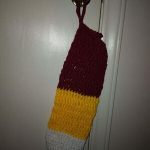 May include: A crocheted stocking with a burgundy, yellow, and white color scheme. The stocking is hanging on a door.