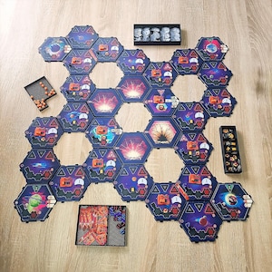 Op de afbeelding: Een bordspel met zeshoekige tegels met ruimte-thema kunstwerken. De tegels zijn gerangschikt op een houten oppervlak, met diverse spelstukken en trays. De tegels hebben afbeeldingen van planeten, ruimteschepen en andere ruimte-gerelateerde objecten. De spelstukken omvatten kleine oranje bollen.