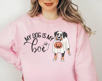 Puede incluir: Sudadera rosa claro con el texto "MY DOG IS MY BOO" y un gráfico de fantasma. También aparece un perro con un disfraz de fantasma y sosteniendo una calabaza. Un divertido diseño temático de Halloween.