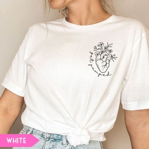 K&ouml;nnte beinhalten: Wei&szlig;es T-Shirt mit einer schwarzen Linienzeichnung eines Herzens, aus dem Blumen wachsen. Der Text "get pumped" ist um das Herz herum geschrieben.