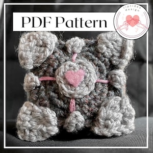 May include: A crocheted gray and pink cube with a heart in the center. The cube is a pattern for a crochet project. The text "PDF Pattern" is at the top of the image.