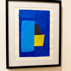 May include: A framed abstract print with geometric shapes in shades of blue, yellow, and brown. The print is set against a white background.