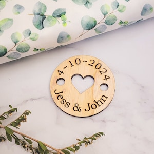 May include: A wooden circle with a heart cut out in the center. The circle is engraved with the text "4-10-2024 Jess & John".