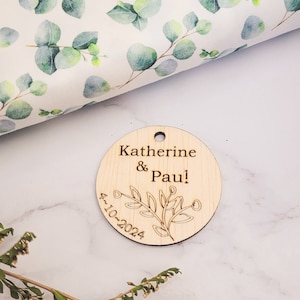 May include: A round wooden tag with the text "Katherine & Paul!" and the date "4.10.2024" engraved on it. The tag features a simple floral design.