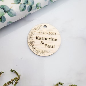 May include: A round wooden tag with a floral design and the text "4-10-2024 Katherine & Paul".