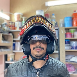May include: A black motorcycle helmet with a red and yellow monster design. The helmet has a clear visor with the text "TSS Twin Shield System" and "Remove this film before use" printed on it.