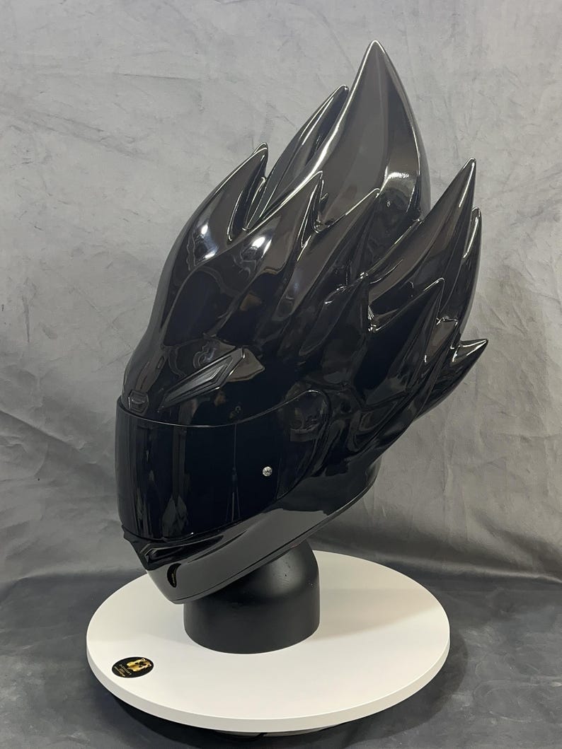 Op de afbeelding: Een glanzend zwarte motorhelm met een uniek, stekelig ontwerp. De helm heeft een donker vizier en wordt gepresenteerd op een witte, cirkelvormige standaard. De algehele esthetiek is futuristisch en edgy.