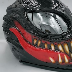 May include: A black motorcycle helmet with a red and white Venom design. The helmet has a clear visor and a black and red paint job.