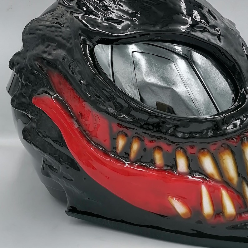 May include: A black motorcycle helmet with a red and white Venom design. The helmet has a clear visor and a black and red paint job.