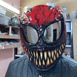 May include: A custom-painted motorcycle helmet in red and black, designed to resemble a monster face with large teeth and reflective lenses. The helmet is worn over a black leather jacket.