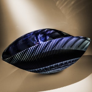 May include: A blue glass bowl with a rippled, textured surface. The bowl is shaped like a seashell and has a dark blue and light blue color pattern.