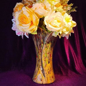 May include: A bouquet of yellow and white roses in a tall, brown and green ceramic vase with a unique, abstract design.