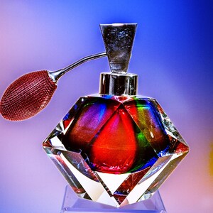 Puede incluir: Un frasco de perfume vintage de vidrio con un diseño facetado. El frasco es rojo, azul y verde con una tapa plateada y un atomizador rojo.