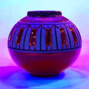 May include: A spherical ceramic vase featuring a matte light gray upper section with dark gray vertical stripes and red metallic accents. The lower half of the vase is finished in a solid, reflective red metallic glaze with a smooth, rounded base.