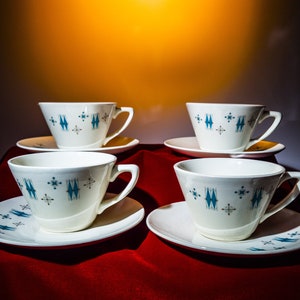 May include: Four white teacups with blue and gray geometric patterns on a red surface. Each cup has a matching saucer.
