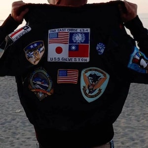 May include: A black bomber jacket with various patches, including a US flag, a Japanese flag, a Taiwanese flag, and a patch that says "Far East Cruise 63-4 USS Galveston".