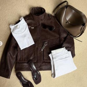 Flat lay outfit featuring a women's vintage brown oversized leather jacket crafted from genuine sheepskin leather, styled with a white t-shirt, white straight-leg jeans, minimalist sandals, sunglasses, and a taupe leather shoulder bag. This retro-inspired leather jacket showcases a relaxed oversized fit, textured pebbled leather finish, utility pockets, and timeless vintage detailing. Perfect for 90s fashion lovers, vintage streetwear enthusiasts, casual luxury outfits, oversized biker jacket
