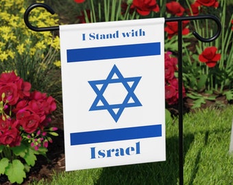Könnte beinhalten: Eine weiße Gartenflagge mit einem blauen Davidstern und dem Text "I Stand with Israel". Die Flagge ist an einem schwarzen Metall-Gartenflaggenhalter befestigt. Die Flagge befindet sich vor einer weißen Holzbank und einem grünen Rasen mit roten Blumen.