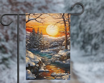 Könnte beinhalten: Eine Gartenflagge im Stil eines Buntglasfensters, die eine Winterszene mit einem Fluss, schneebedeckten Bäumen und einer großen orangefarbenen Sonne darstellt, die hinter den Bäumen untergeht.