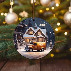 Könnte beinhalten: Ein runder Weihnachtsbaumschmuck mit einer verschneiten Szene eines Hauses mit Lichtern, einem Lieferwagen und dem Text "2023" und "Danke".