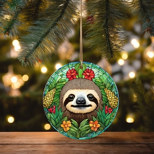 May include: A round Christmas ornament featuring a stained glass style illustration of a sloth with green leaves, red flowers, and yellow pineapples.