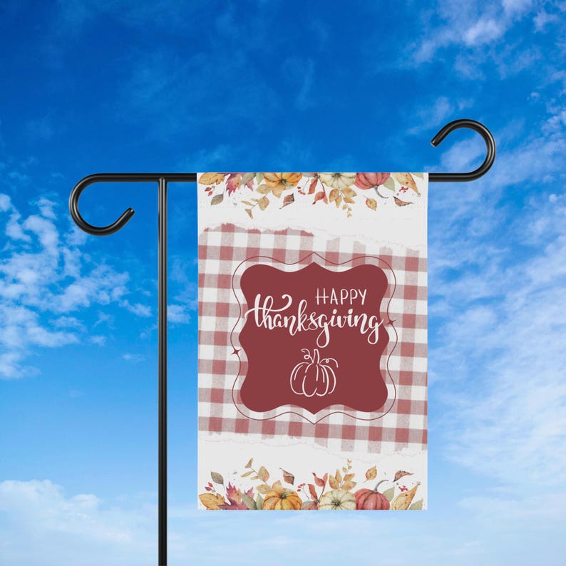 K&ouml;nnte beinhalten: Eine rechteckige Gartenflagge mit einem rot-wei&szlig; karierten Muster und einem weinroten zentralen Design. Das Design zeigt die Worte "Happy Thanksgiving" in Schreibschrift und eine K&uuml;rbisillustration. Florale und K&uuml;rbisakzente zieren die oberen und unteren R&auml;nder.