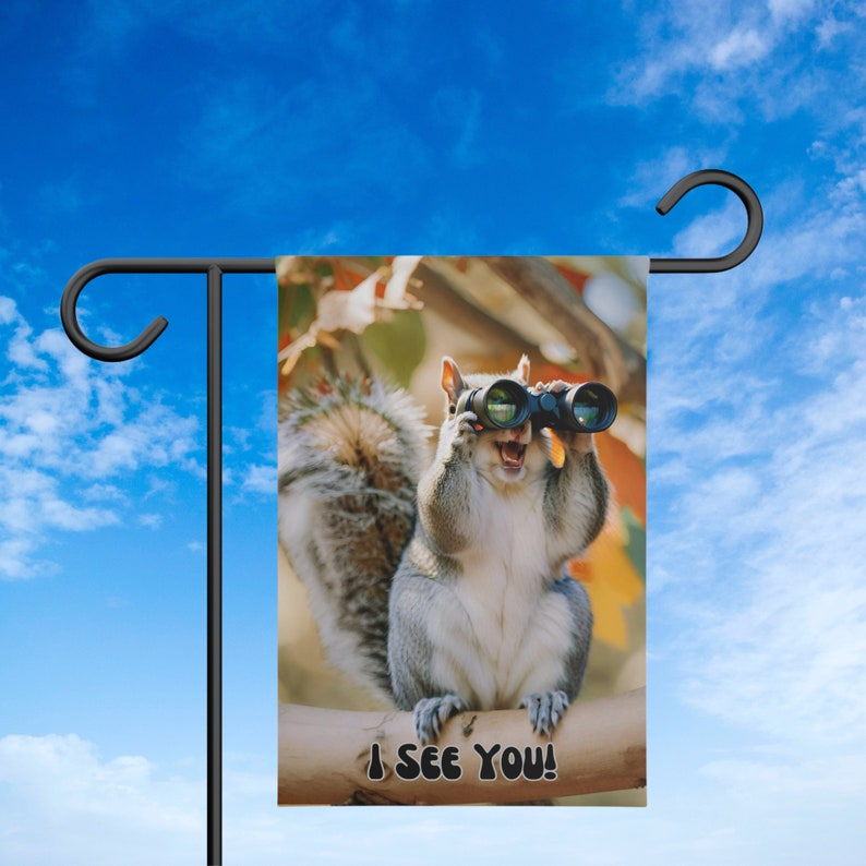 May include: A gray squirrel with a bushy tail holds binoculars and looks directly at the viewer. The squirrel is sitting on a branch with the text "I SEE YOU!" below it.