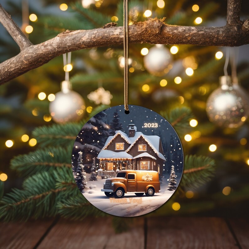 Op de afbeelding: Een ronde kerstbal met een besneeuwde sc&egrave;ne van een huis met lichtjes, een bestelwagen en de tekst "2023" en "Bedankt".