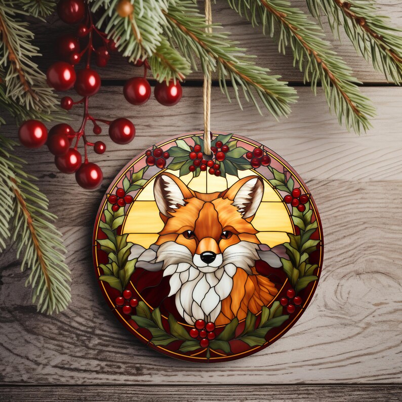 May include: A round glass ornament with a stained glass design of a fox's face surrounded by holly and red berries.