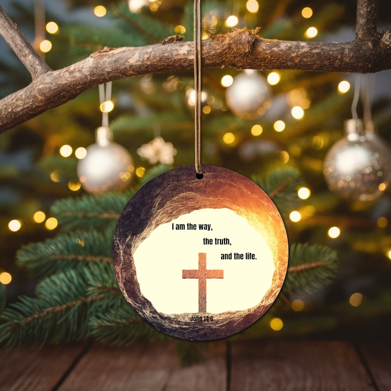 May include: A round, wooden Christmas bauble with a rustic, textured surface. The bauble features a white background with a brown cross and the text "I am the way, the truth, and the life. John 14:6".