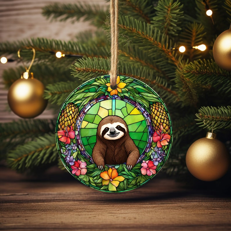 May include: A round, stained glass Christmas ornament featuring a sloth with a green, yellow, and orange floral design. The sloth is brown and has a happy expression.