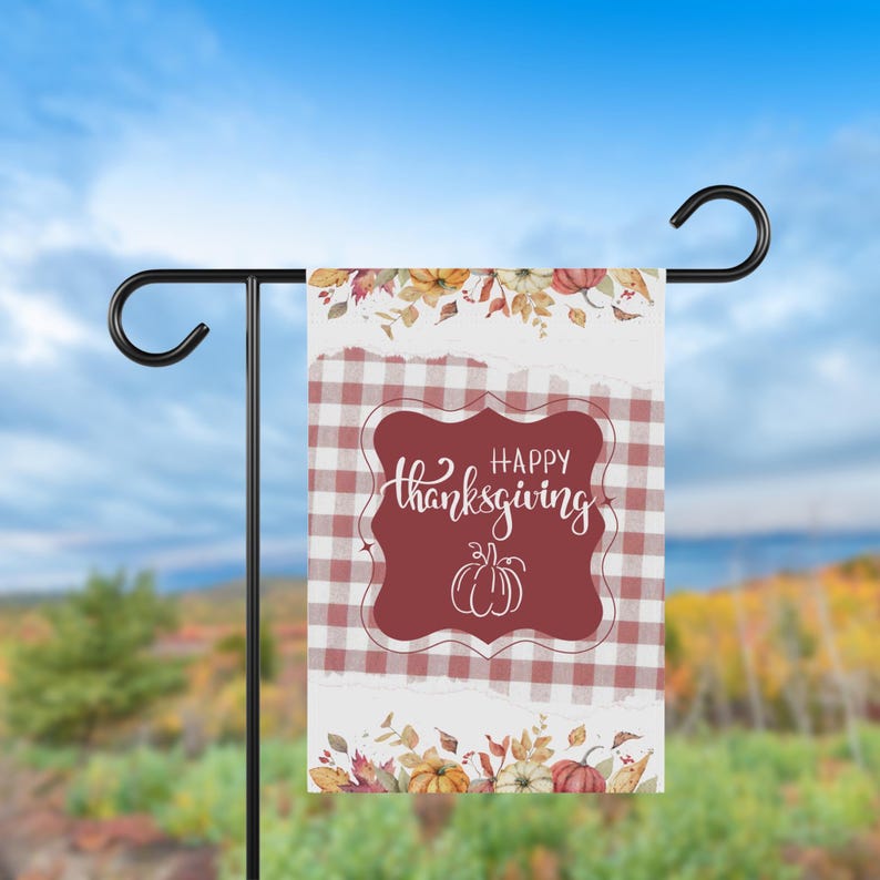 K&ouml;nnte beinhalten: Eine Thanksgiving-Gartenflagge mit einem rot-wei&szlig; karierten Muster und einem weinroten zentralen Design. Das Design zeigt die Worte "Happy Thanksgiving" in Schreibschrift und eine wei&szlig;e K&uuml;rbisillustration. Florale Akzente in Herbstfarben schm&uuml;cken die Ober- und Unterseite.