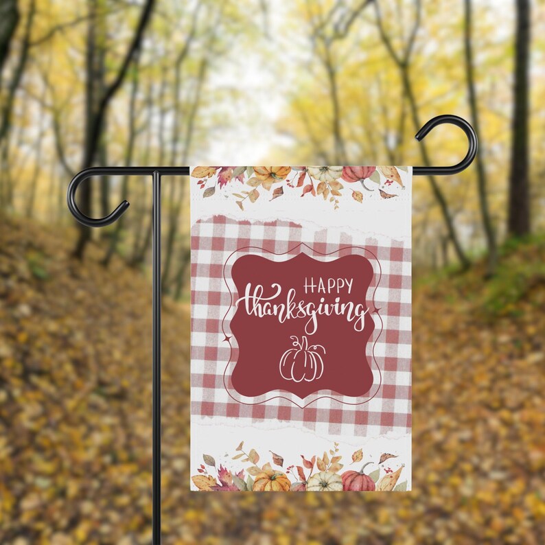 K&ouml;nnte beinhalten: Eine Gartenflagge mit Thanksgiving-Motiv. Die Flagge zeigt ein rot-wei&szlig; kariertes Muster mit einem weinroten zentralen Design mit der Aufschrift "Happy Thanksgiving" und einer K&uuml;rbisillustration. Florale und K&uuml;rbis-Akzente zieren die Ober- und Unterseite.