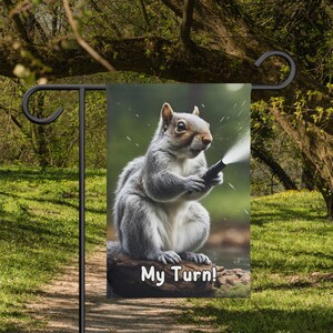May include: A gray squirrel holds a garden hose and looks at the camera. The squirrel is sitting on a log with the text "My Turn!" printed on it.