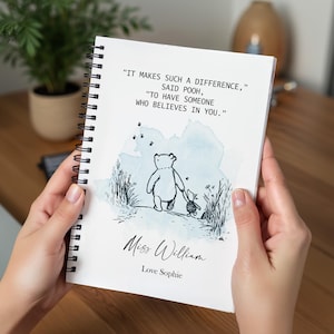 Può includere: Un taccuino a spirale bianco con un'illustrazione a inchiostro nero di Pooh e Pimpi che camminano. La copertina include il testo: "It makes such a difference," said Pooh, "to have someone who believes in you." Mostra anche "Miss William" e "Love Sophie" in nero su uno sfondo ad acquerello azzurro.
