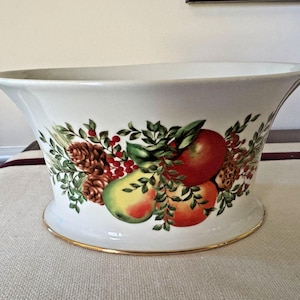 May include: White ceramic planter with a gold rim, decorated with a colorful fruit and foliage design. The illustration includes apples, pears, pinecones, and berries. The planter has a flared shape.