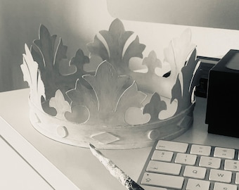 May include: A white paper crown with intricate details, sitting on a white surface next to a keyboard and a paintbrush.