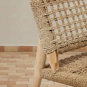 May include: Close-up of a woven chair with a natural, light brown color. The chair features a grid-like pattern on the backrest and seat, with wooden legs. The woven material appears to be made of natural fibers.