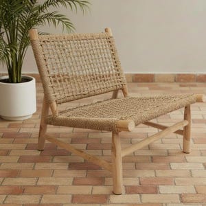 May include: A natural-toned woven rope chair with a wooden frame. The chair features a rectangular back and seat, with the rope woven in a grid pattern. The chair is set on a brick-paved surface, with a potted plant in the background.