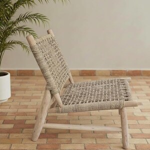May include: A light-colored wooden chair with a woven seat and back. The chair has a simple design with four legs and a slatted back. The woven material is a neutral beige color, and the wood has a natural finish.