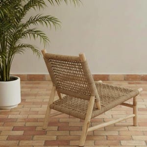 May include: A woven rope chair with a light wood frame. The chair has a woven seat and backrest, and is set against a neutral background. A potted plant is visible in the background.